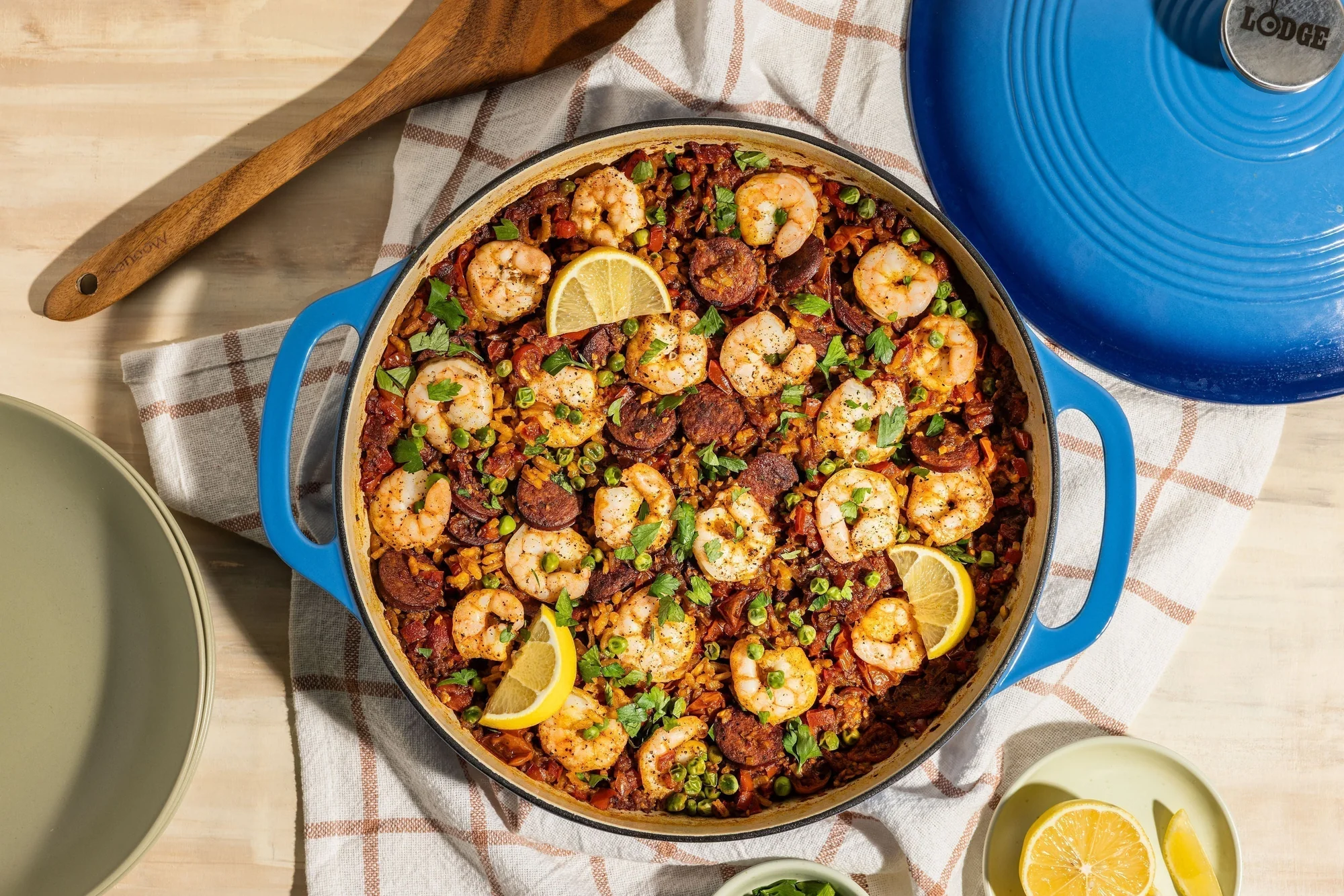 Domaća paella s kozicama i kobasicom pripremljena u plavoj niskoj posudi od emajliranog lijevanog željeza.