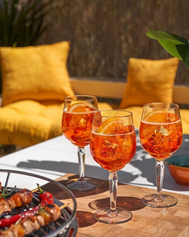 Tri čaše ljetnog koktela Aperol Spritz s ledom i narančom poslužene na terasi